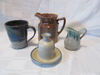 Group photo of four assorted Canadian pottery items: brown pitcher, bud vase with plate, creamer, and mug