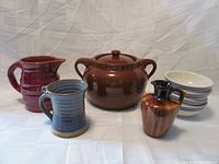 Full view of Lot showing all six items: brown bean pot with lid, four white dessert bowls stacked, blue ribbed milk pitcher, brown striped mug and small brown syrup jug.
