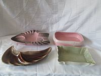 Four ceramic items displayed on a white fabric backdrop: two flower bowls, one ashtray, one dish.