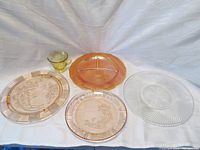 Photo showing all five items in the lot: amber and pink plates with floral patterns, amber creamer, and clear crystal sandwich plate with spiral design.