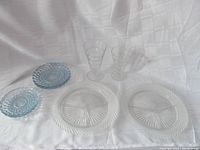 Full view of all glassware items on white fabric background showing both plates, tumblers, salad plates, and saucers.