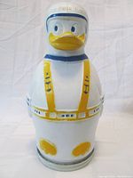 Front view of the Donald Duck plastic cereal bank showing the painted facial features, yellow buckles, and blue rimmed helmet with white background.