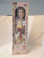 Porcelain doll in original floral box with clear display window showing the doll fully dressed in Victorian outfit.