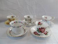 Five teacup and saucer sets arranged together showcasing varying floral patterns and gold trim, no visible chips or cracks