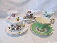 Five Royal Albert teacup and saucer sets arranged on a fabric backdrop, showing various floral patterns and colors including green and pastel shades, no visible wear or damage.