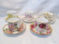 Five teacup and saucer sets each with distinctive floral patterns and gold trim, arranged together to show overall lot contents