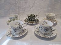 Five Royal Albert teacups and saucers displayed as sets on a white fabric background showing their floral patterns and shape.