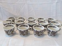Front view of all 14 white ceramic mugs with brown floral design arranged in rows to show quantity and pattern.