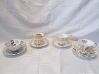 Four Queen Anne teacup and saucer sets displayed side by side showing different floral patterns and trims.