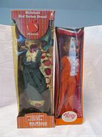 Photo of two boxed porcelain dolls: left is Rob McIntosh Anne of Green Gables doll with tartan themed packaging; right is 14-inch Winny doll in orange outfit.