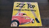 Front view of vinyl single sleeve featuring ZZ Top 'Gimme All Your Lovin' artwork with a pink classic car and woman's leg with shoe.