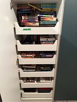 Six white pull-out shelves packed with various young adult fiction books, hardcover and paperback, showing colorful spines and assorted titles.