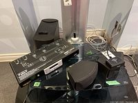 Lot showing Bose Acoustimass module with satellite speakers, Monster Power HTS 1600 power conditioner, remote, and power adapter on black table surface near wall outlets.