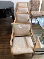 Four identically upholstered wood frame chairs lined up next to each other showing pattern and armrests