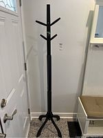 Full view of the black wooden coat tree standing at 72 inches tall near a door.