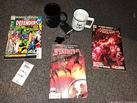 Overview of three Marvel comics and two mugs on carpeted floor