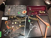 Main overview of lot with multiple pieces of costume jewelry including necklaces, bracelets, watches, and two hangers on black table