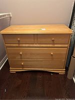 Front view of the light-colored wooden dresser with three drawers and wooden knobs.