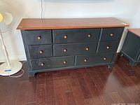 Front view of eight drawer wooden dresser showing the black painted base and natural wood top with wooden knobs on drawers.