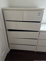 Front view of white MDF dresser with six drawers, showing drawer alignment and overall condition.