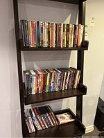 Three shelves of DVDs stacked in rows on a dark wood shelf unit.