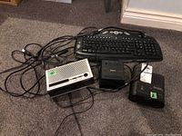 Top view of two alarm clock radios, Sony cassette player, and keyboard with tangled cords on carpet