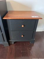 Front view of the two drawer end table showing the natural wood top and black base with wooden knobs on drawers.