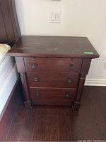 Side view of one Kincaid end table showing three drawers, column details, dark wood, and visible wear on top.
