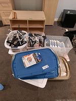 Photo showing plastic baskets filled with various hangers and stackable storage bins with lids in blue, beige, and white colors.