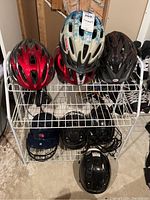 Overview of eight helmets on a white rack showing four bike helmets on top shelf, three black CCM hockey helmets and one Rawlings batting helmet on bottom shelf.