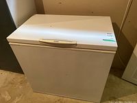 Front and top view of white Kenmore chest freezer with a handle on the top lid, placed in a basement area.