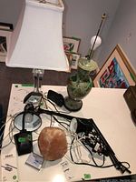 Photo of two lamps (one clear glass with white shade and one ceramic floral) and a Himalayan salt lamp on a table with cords and other accessories.