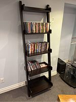 Front view of dark brown wooden shelf with five fixed shelves holding DVDs and CDs