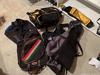 Photo showing multiple sports bags on the floor including a black and orange gym bag, vintage racket bag, large ski bag, yellow golf bag, and aluminum crutches.