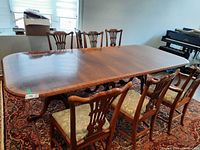 Full angled view of the rectangular wood dining table with 6 chairs around it in a room with carpet flooring and a window.