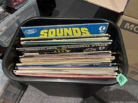 View of a bin filled with numerous vinyl records, showing their spines and some album covers on top