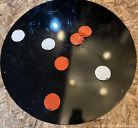 Top view of round black magnetic bulletin board with six circular red and white magnets attached.