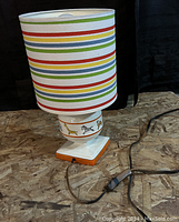 Full lamp including ceramic base decorated with zoo animals and colorful striped shade, sitting on wood surface.