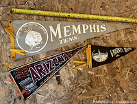 Three vintage travel pennants laid flat on a wood surface, showing designs for Memphis, Arizona, and Virginia Beach.