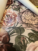 Rolled wallpaper showing large floral graphics with detailed pink, cream, and mauve roses and foliage.