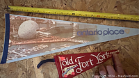 Photo showing two vintage pennants: Ontario Place and Old Fort York Room, laid side by side on a plywood surface with measuring tape