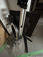 Photo showing silver and black tripod with circular ring light mounted, black monopod, and carrying accessories on floor