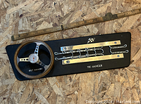 Image showing a race car steering wheel style belt hanger and a metal tie hanger attached to a wooden plaque, with a ruler for scale.