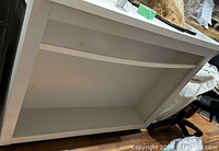 View of the underside and interior bottom shelf of white rolling retail display unit, showing structure and condition including minor marks.