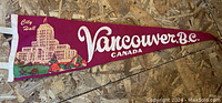 Image of vintage maroon felt pennant depicting City Hall and text reading Vancouver B.C. Canada on a wooden floor background.