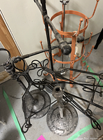 Photo showing black metal book stands and easels with decorative scrollwork alongside orange cylindrical cup rack with multiple hooks.