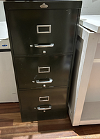 Full front view of the vintage black steel filing cabinet showing three drawers with handles, locks, and label holders.