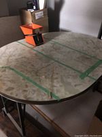Top view of oval vintage Formica diner table showing worn cream/beige patterned surface with green tape marks and one orange object on top