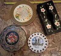 Top-down image of four items: three decorative plates and one floral painted dark-colored box (Kleenex box cover).