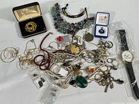 Wide view of assorted costume jewelry including multiple necklaces, rings, brooch, watch, and earrings laid out on surface.
